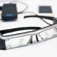 Μέχρι το 2030 τα έξυπνα γυαλιά θα μπορούν να μας «τηλεμεταφέρουν» σε διαφορετικές τοποθεσίες, υπόσχεται ο ιδρυτής του Facebook, Μαρκ Ζούκερμπεργκ. Ένα ζευγάρι προηγμένα «έξυπνα γυαλιά» που θα επιτρέπουν στις προσωπικές συναντήσεις να αντικατασταθούν από μια ψηφιακή εμπειρία, ετοιμάζει το Facebook. Πρόκειται για μια τεχνολογία επαυξημένης πραγματικότητας, η οποία θα παρουσιάζει γραφικά που δημιουργούνται από υπολογιστή σε εικόνες του πραγματικού κόσμου. Σύμφωνα με δηλώσεις του Μαρκ Ζούκερμπεργκ, που έγιναν την περασμένη Δευτέρα, μια τέτοια τεχνολογία όχι μόνο θα περιόριζε την ταλαιπωρία των μετακινήσεων, αλλά θα μείωνε τη ρύπανση που προκαλούν οι μετακινήσεις στο περιβάλλον. «Προφανώς, θα συνεχίσουμε να βρισκόμαστε σε αυτοκίνητα και αεροπλάνα και όλα αυτά. Όμως, όσο περισσότερο μπορούμε να τηλεμεταφερόμαστε, όχι μόνο ελαττώνουμε τις μετακινήσεις αλλά νομίζω ότι κάνουμε καλό στην κοινωνία τον πλανήτη συνολικά», υπογράμμισε ο διευθύνων σύμβουλος του Facebook. Ο ίδιος πιστεύει ότι, μέχρι το 2030, η εταιρεία του θα έχει καταφέρει να κατασκευάσει ένα ζευγάρι γυαλιών με κανονική εμφάνιση, τα οποία μπορούν να δίνουν στο χρήστη την εντύπωση ότι έχει μεταφερθεί πραγματικά σε άλλο χώρο. «Αντί να κάνετε μια βιντεοκλήση, απλά θα κινείτε τα δάχτυλά σας και θα τηλεμεταφέρεστε. Θα νιώθετε ότι είστε στ’ αλήθεια στον ίδιο χώρο με τους φίλους σας, θα τους βλέπετε να κάθονται στον καναπέ σαν να ήταν δίπλα σας», είπε ο Ζούκερμπεργκ.