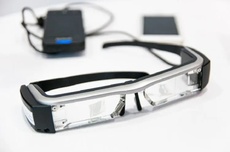Μέχρι το 2030 τα έξυπνα γυαλιά θα μπορούν να μας «τηλεμεταφέρουν» σε διαφορετικές τοποθεσίες, υπόσχεται ο ιδρυτής του Facebook, Μαρκ Ζούκερμπεργκ. Ένα ζευγάρι προηγμένα «έξυπνα γυαλιά» που θα επιτρέπουν στις προσωπικές συναντήσεις να αντικατασταθούν από μια ψηφιακή εμπειρία, ετοιμάζει το Facebook. Πρόκειται για μια τεχνολογία επαυξημένης πραγματικότητας, η οποία θα παρουσιάζει γραφικά που δημιουργούνται από υπολογιστή σε εικόνες του πραγματικού κόσμου. Σύμφωνα με δηλώσεις του Μαρκ Ζούκερμπεργκ, που έγιναν την περασμένη Δευτέρα, μια τέτοια τεχνολογία όχι μόνο θα περιόριζε την ταλαιπωρία των μετακινήσεων, αλλά θα μείωνε τη ρύπανση που προκαλούν οι μετακινήσεις στο περιβάλλον. «Προφανώς, θα συνεχίσουμε να βρισκόμαστε σε αυτοκίνητα και αεροπλάνα και όλα αυτά. Όμως, όσο περισσότερο μπορούμε να τηλεμεταφερόμαστε, όχι μόνο ελαττώνουμε τις μετακινήσεις αλλά νομίζω ότι κάνουμε καλό στην κοινωνία τον πλανήτη συνολικά», υπογράμμισε ο διευθύνων σύμβουλος του Facebook. Ο ίδιος πιστεύει ότι, μέχρι το 2030, η εταιρεία του θα έχει καταφέρει να κατασκευάσει ένα ζευγάρι γυαλιών με κανονική εμφάνιση, τα οποία μπορούν να δίνουν στο χρήστη την εντύπωση ότι έχει μεταφερθεί πραγματικά σε άλλο χώρο. «Αντί να κάνετε μια βιντεοκλήση, απλά θα κινείτε τα δάχτυλά σας και θα τηλεμεταφέρεστε. Θα νιώθετε ότι είστε στ’ αλήθεια στον ίδιο χώρο με τους φίλους σας, θα τους βλέπετε να κάθονται στον καναπέ σαν να ήταν δίπλα σας», είπε ο Ζούκερμπεργκ.